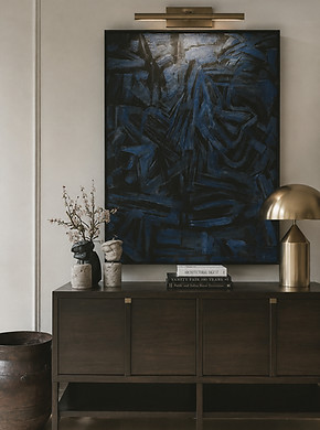Dark wood console table with blue abstract artwork, brass picture light, and styled decorative accents