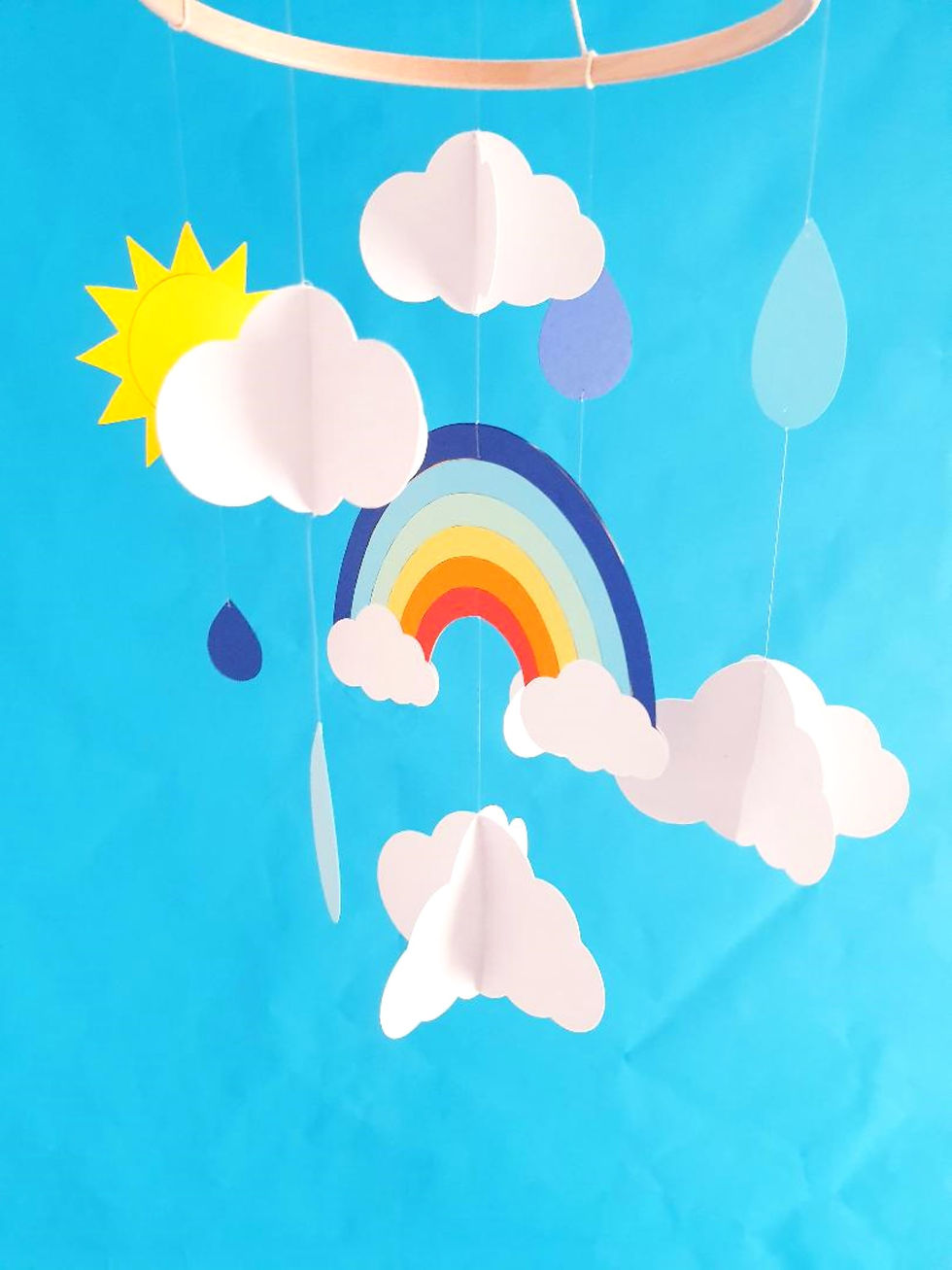 Mobile décoratif suspendu dans une chambre d’enfant. Apporte une touche poétique et colorée grâce à son thème ciel : nuages,