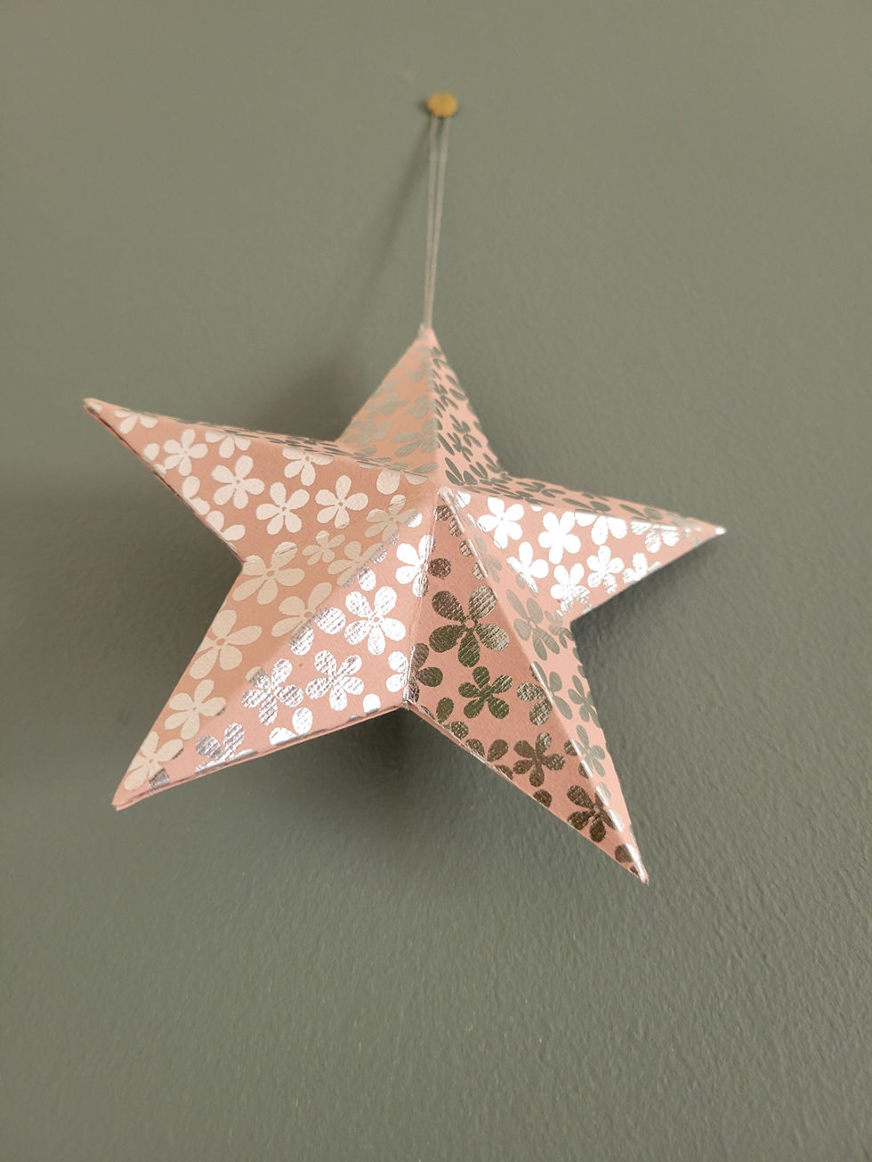 Étoile 3D en papier recyclé rose métallisé suspendue pour décoration de sapin de Noël.