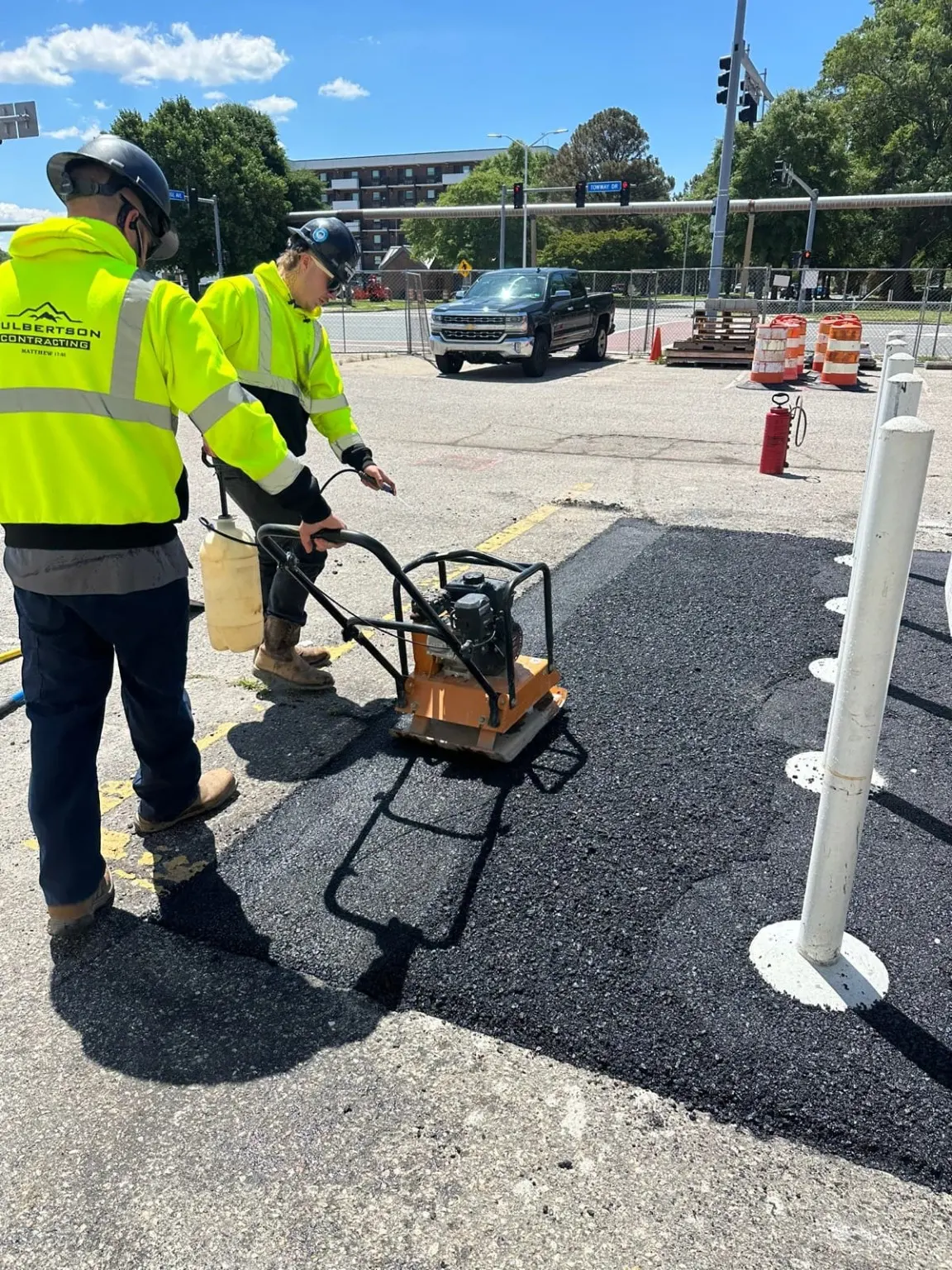 Workers in Culbertson-branded high-visibility clothing compact an asphalt patch.