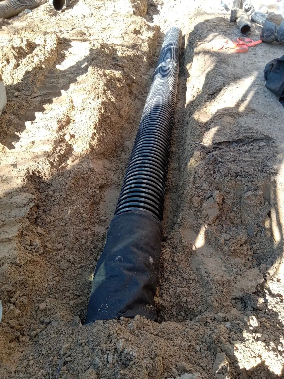 Black corrugated drainage pipe placed in an excavated trench.