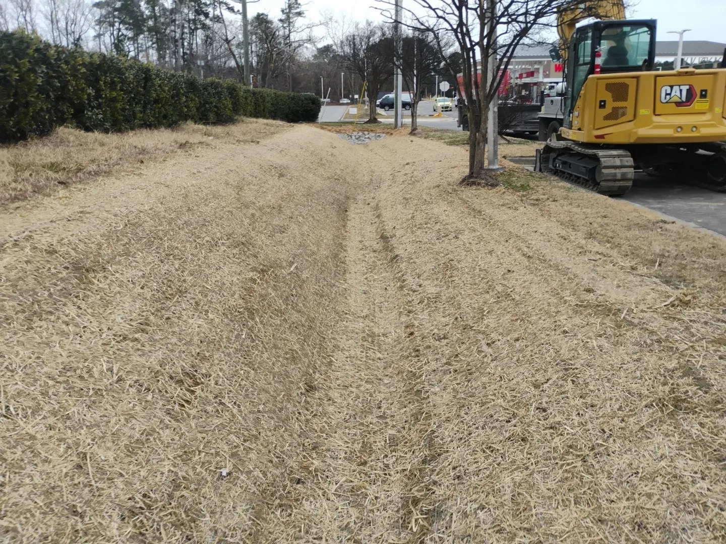 A straw-covered drainage swale with construction equipment alongside it.
