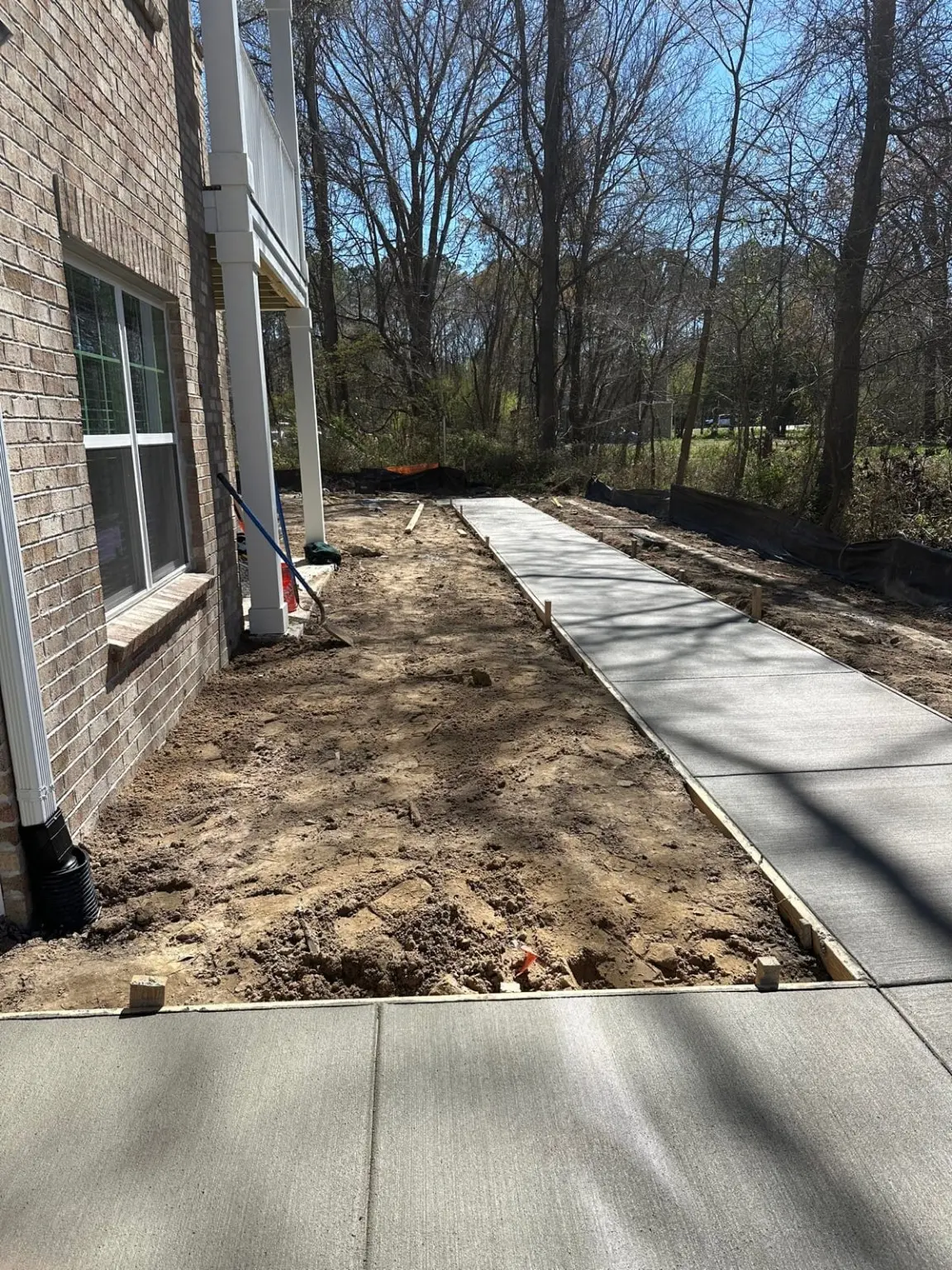 New concrete walkways beside a building while surrounding site work continues.
