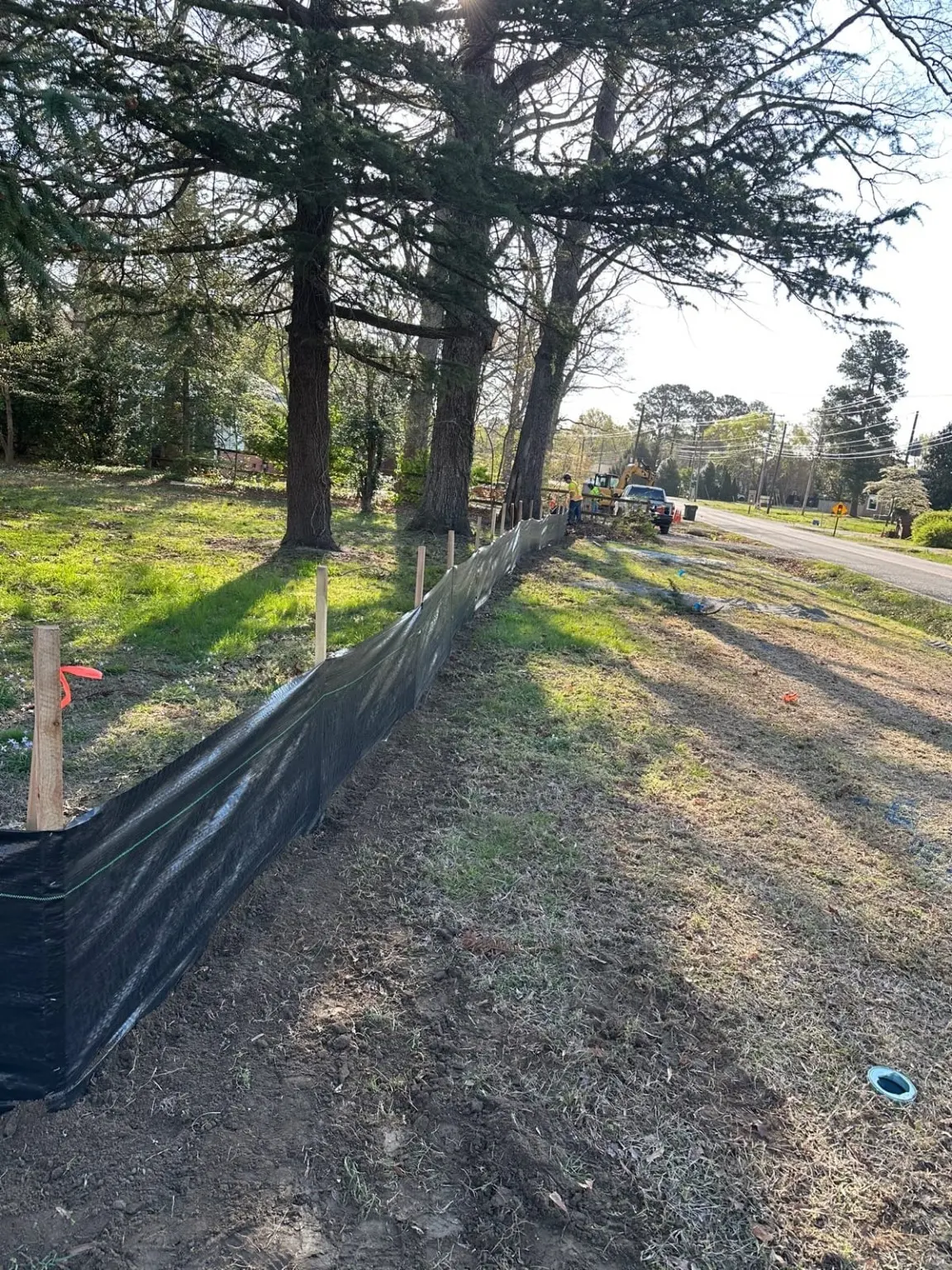 Black silt fence along a tree-lined construction work area.