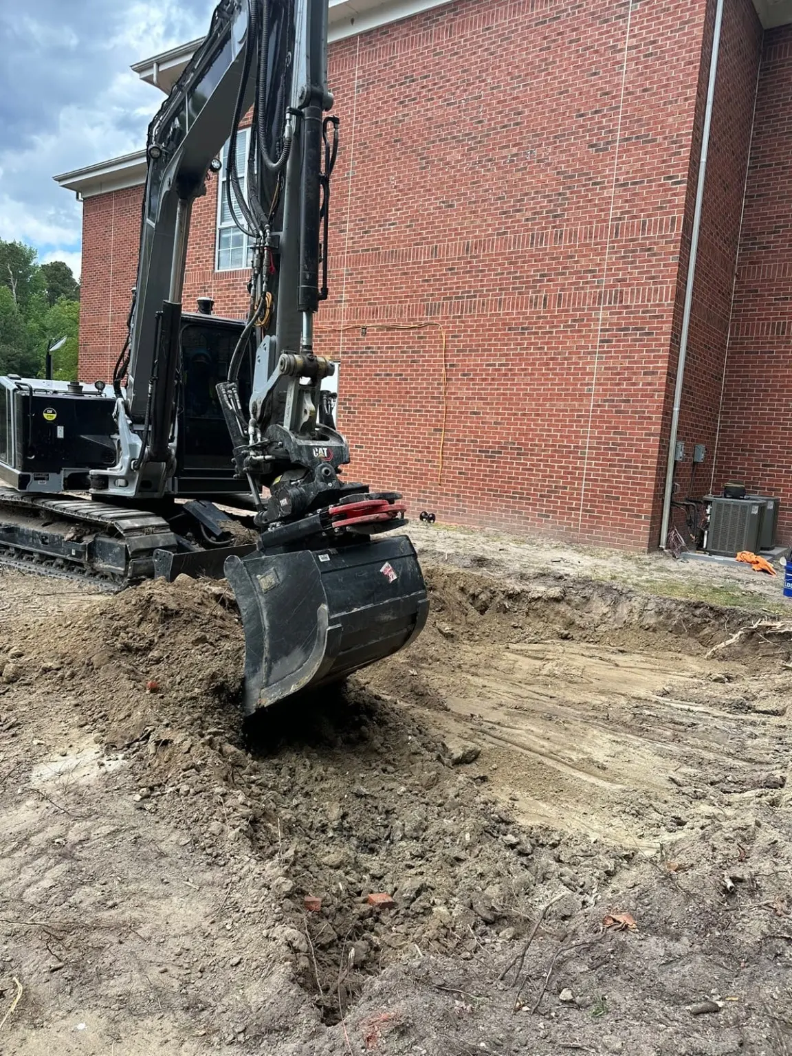A black excavator with a grading attachment beside a brick building.