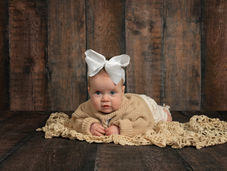Baby girl posed in neutral colors with a big bow for tummy time milestone photography