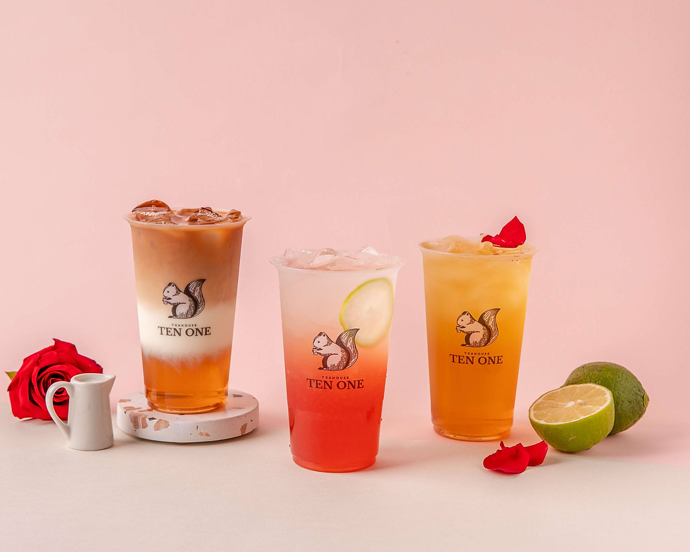 A selection of tea beverages in front of a pink background garnished with fruits and flowers.