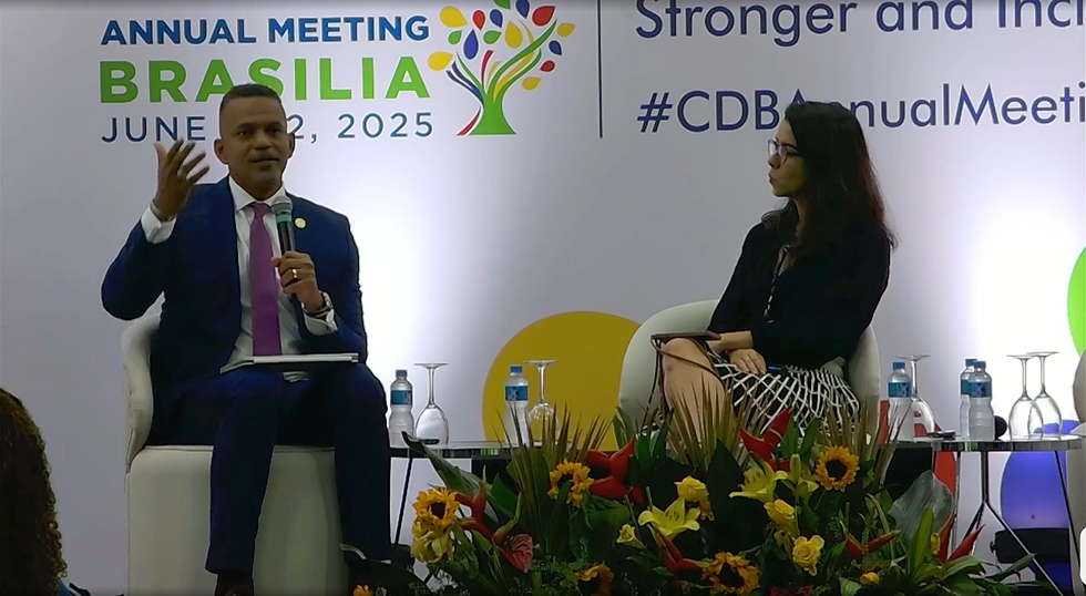 darkskinned man wearing a suit is talking and gesticulating into a microphone while a fair woman sits beside him