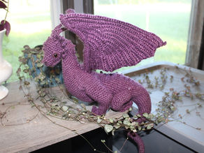A purple Crochet dragon on a grey tabletop with vines surrounding it