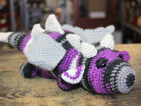 A grey, purple, and black dragon laying on a wooden tabletop.