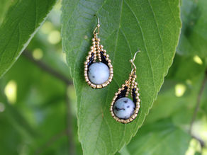 A pair of grey quartz earrings with a black and gold beaded basket holding the stones.