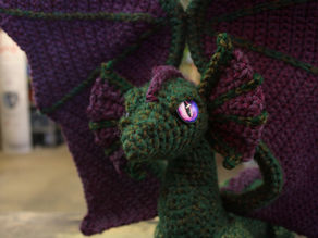 A Green crochet dragon with purple frills and a glowing purple eye.