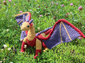 a red orange and purple crochet dragon in the grass.