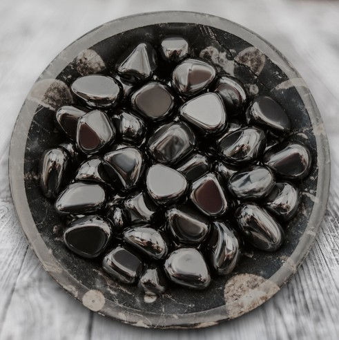 Pierres roulées en hématite AB du Brésil, aux reflets gris métalliques brillants, présentées dans une coupelle sombre