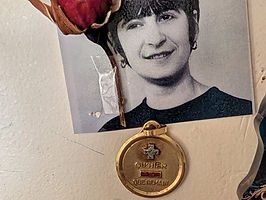 Photographie en noir et blanc de Marcelline, accompagnée d'une rose séchée et de sa médaille d'amour en or, souvenir familial.