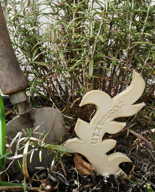 Handgetöpferter winterharter Kräuterstecker aus Keramik mit eingedrücktem Schriftzug "Rosmarin" im Kräuterbeet platziert.