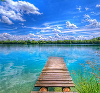Wooden dock extending into serene turquoise lake under bright blue sky with clouds, peaceful nature landscape