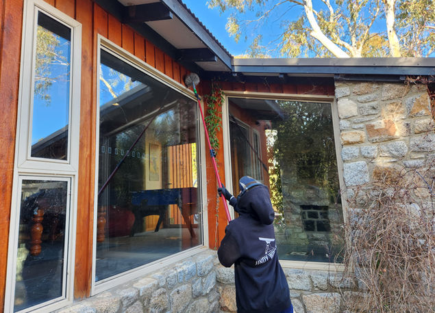 Cleaning technician removing cobwebs from the eaves of a house