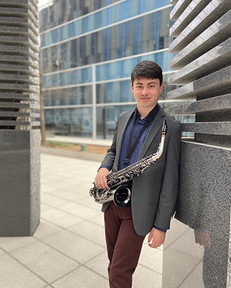 Carlos Taboada holding an alto saxophone and leaning on a structure in the Dallas Art District.