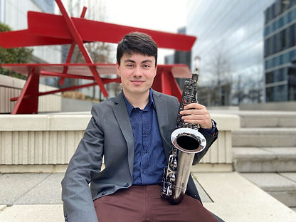 Carlos Taboada holding a saxophone and sitting on a staircase in the Dallas Art District.