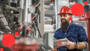 The image is titled "Steam Boiler Maintenance Tips for Coal-Fired Systems" and serves as a promotional graphic. It depicts a worker wearing a red hard hat and a blue shirt, holding a tablet displaying the "National Coal Suppliers" logo along with the text "Quality Coal Products." The background features industrial equipment, including pipes, valves, and machinery, suggesting a coal-fired system environment. Red circular design elements with a dotted pattern are overlaid to enhance the visual appeal.