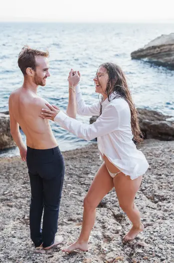 Couple heureux sur la plage, riant et tenant les mains près de l'océan.