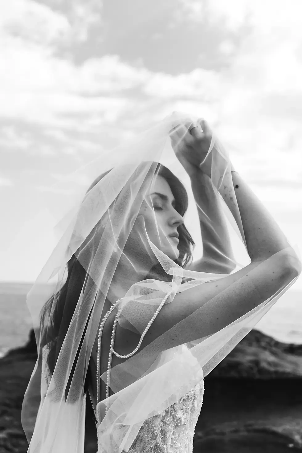 Hermosa novia con velo, posando con el viento frente a un paisaje marino.
