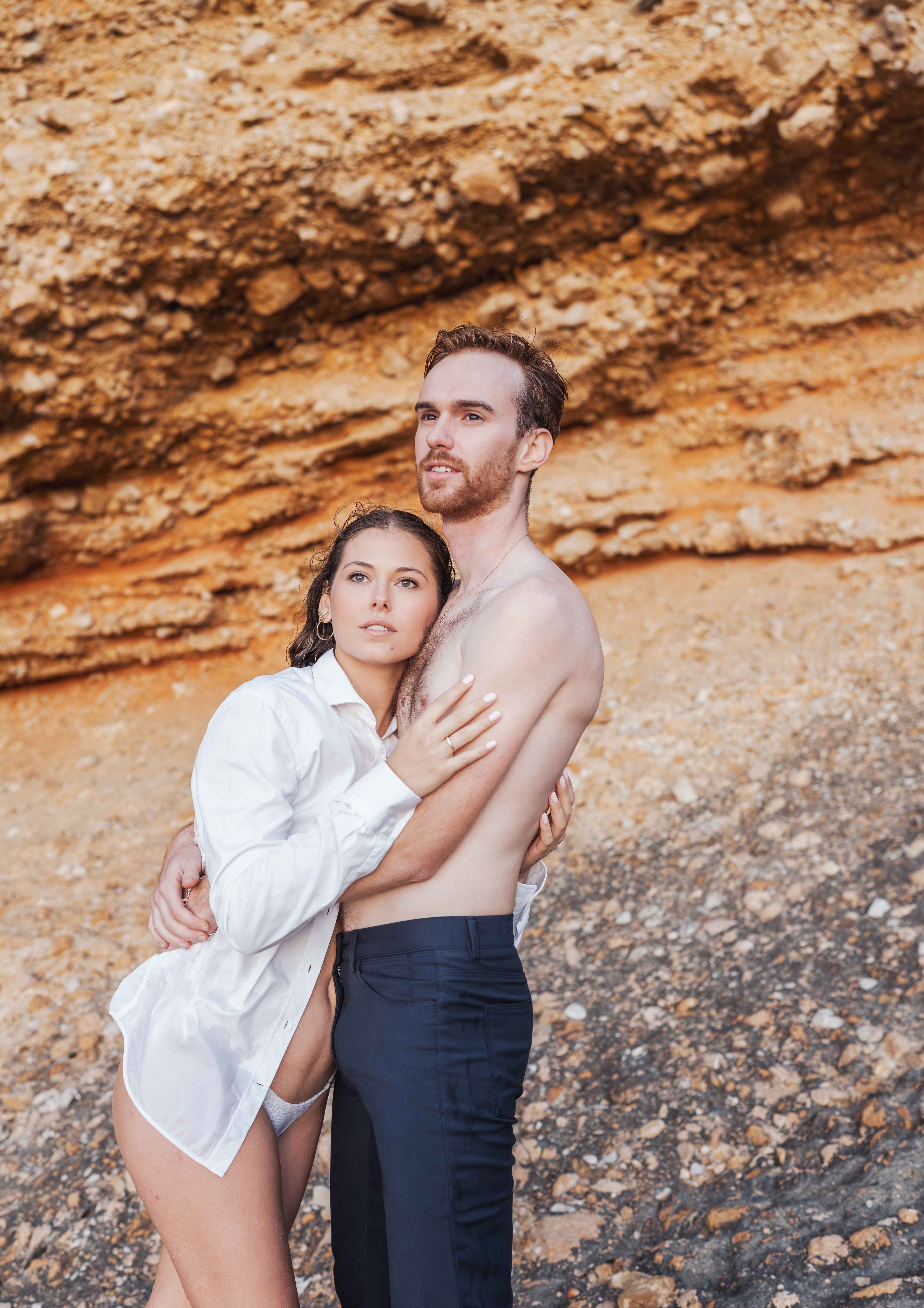 Couple embracing each other, looking away from the camera, on a rocky background.