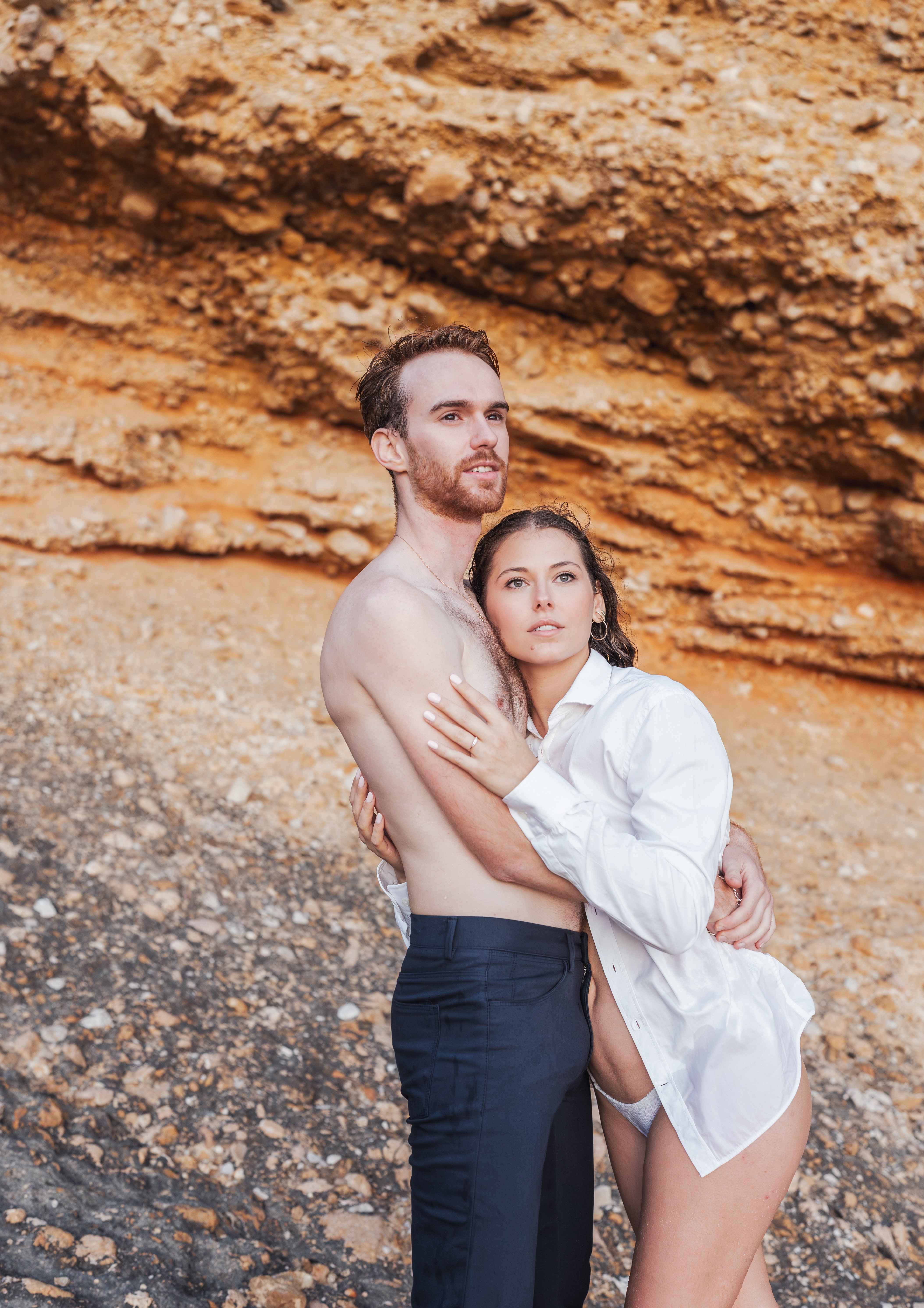 Couple embracing each other, shirtless man, white shirt, rock background, togetherness.