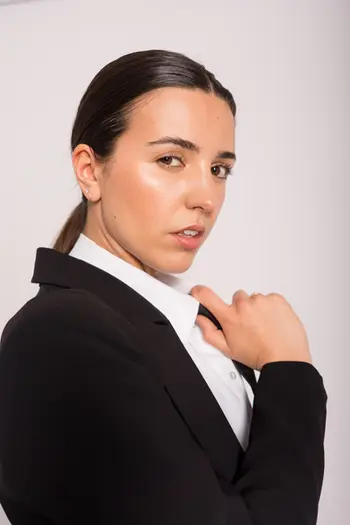 Donna in abito nero, camicia bianca, posa professionale e seria. Sfondo chiaro.