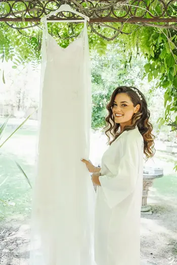 Smiling bride with hanging wedding dress, Wedding Portfolio - Camille & Kevin, garden.