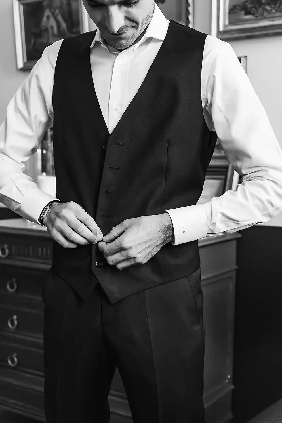 Homme ajuste son gilet noir avec chemise blanche, préparation vestimentaire avant événement.