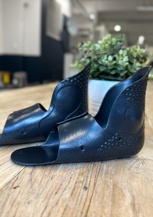 Close-up of the smooth ankle openings and curved upper profiles of two black TPU inserts beside a plant.