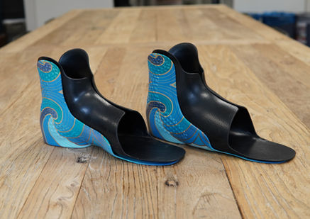 Pair of blue patterned AFOs fitted with black TPU inserts in three-quarter view on a wooden table.