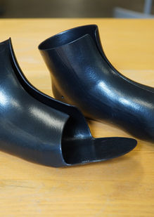 Pair of black TPU inserts in three-quarter view on a warm wooden surface, with both footplates visible.