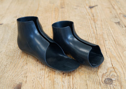 Pair of black TPU inserts angled together on a wooden table, showing both ankle contours and footplates.