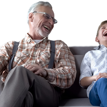 Old man and young boy sitting on the couch laughing.