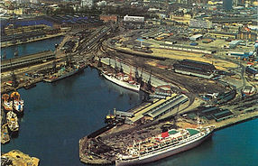 Aerial view of Reina del Mar berthed in harbour beside dock buildings and railway yards