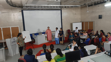 A teaching hall with several participants sitting and standing and Sonali at the whiteboard in front.