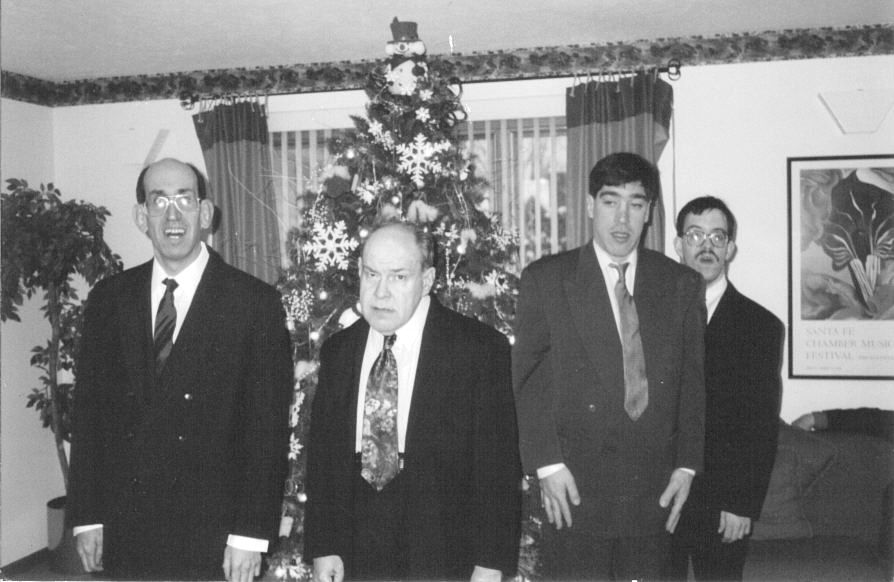 Four men in suits standing in front of a Christmas tree