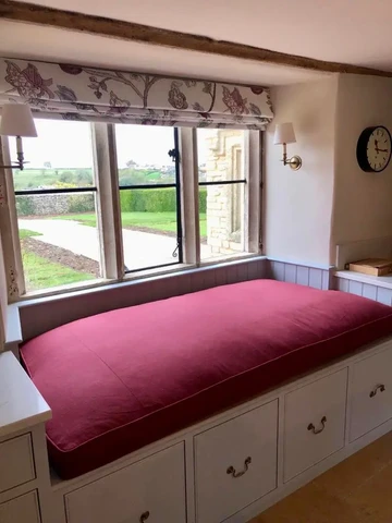 A window seat with large luxury red cushion.