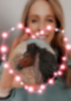 Artist DeeAnn Kjelshus, facing camera holding out a medallion she painted red rain with a filter effect of a pink lit up heart in front.