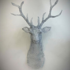 Hand-crafted architectural animal sculpture titled White Stag (2023) by Marina Berlin. An intricate wire wall-mounted art piece made of woven metal mesh, casting delicate geometric shadows on a gallery wall.