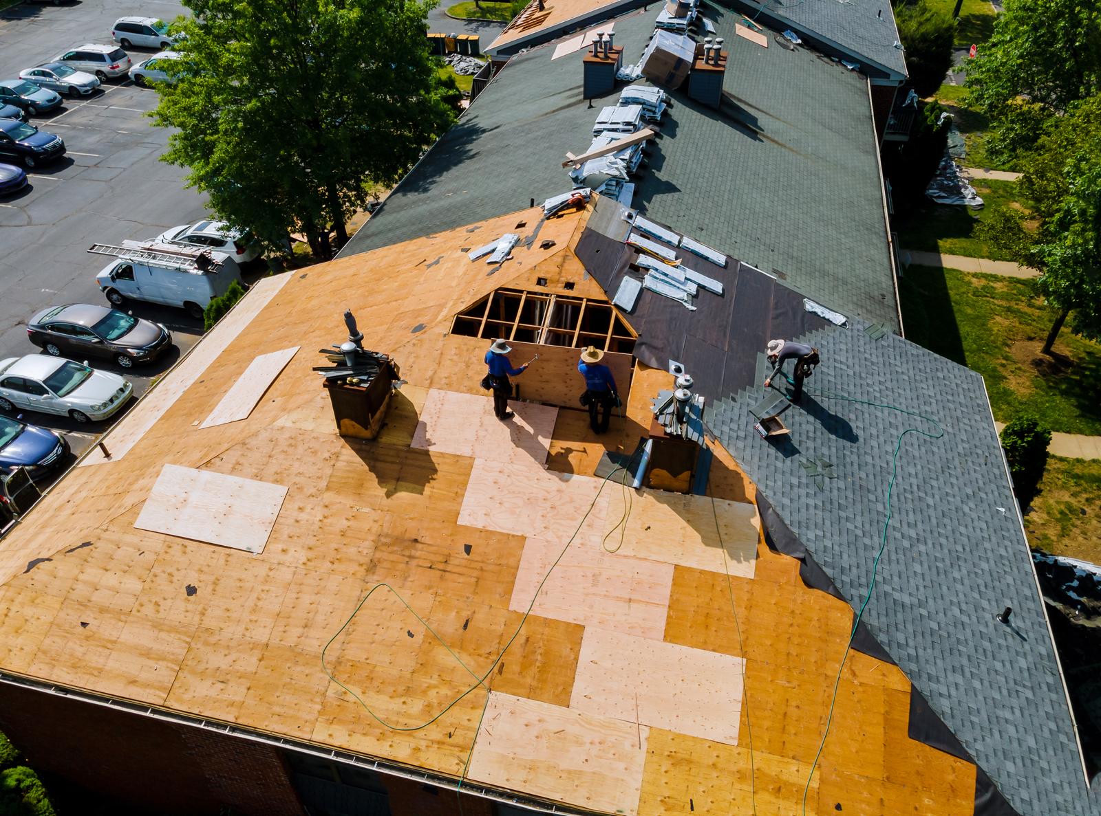Aerial view of roof decking and shingles being replaced, with crew members at work.