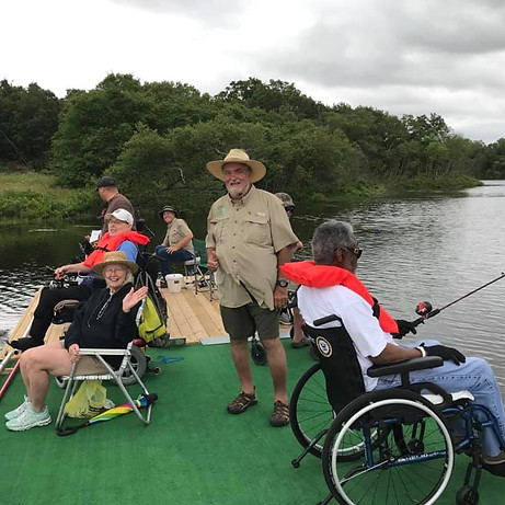 A group of people sitting in chairs and wheelchairs fish on the docks in the middle of the lake.
