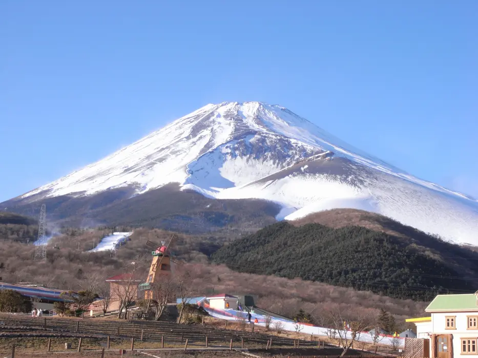 Mt. Fuji in winter snow seen from the Fujiyama Snow Resort Yeti base, with windmill and resort buildings.
