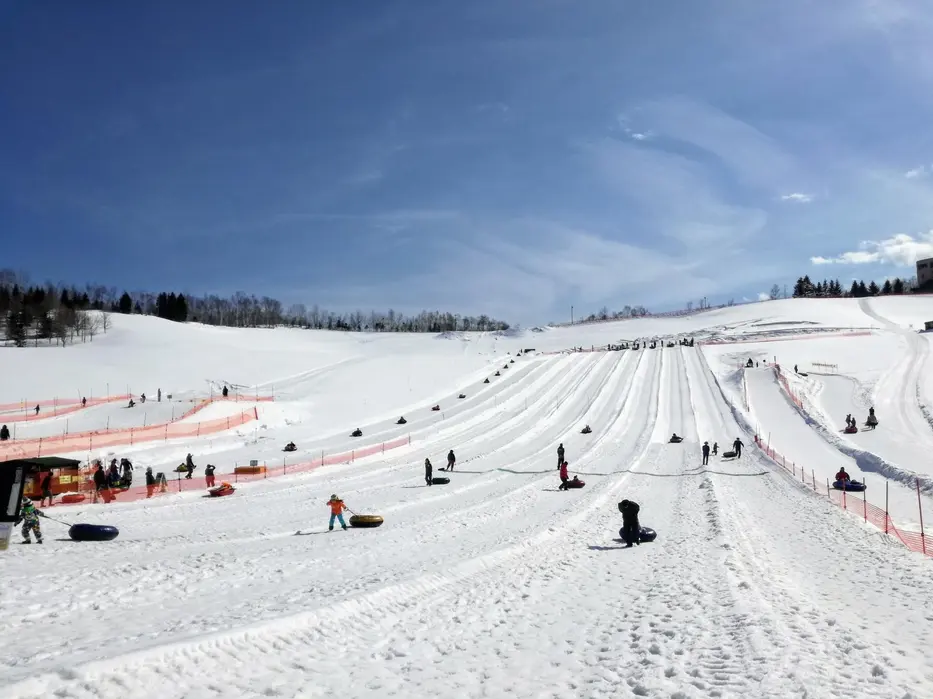 Children and families snow tubing down dedicated lanes at Yeti Snow Resort under a bright blue sky.