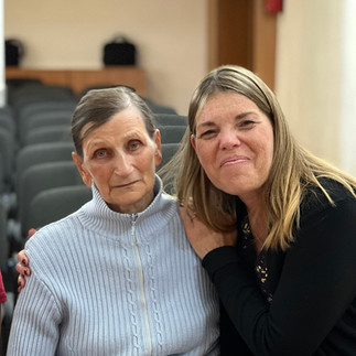 A younger lady sits with her arm around an older woman in a church sanctuary