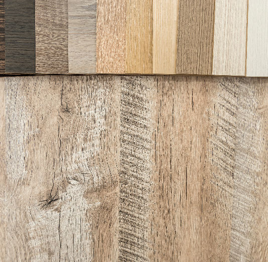 Various wood laminate samples in dark to light shades are arranged over a large wood panel, showcasing color and texture contrast.