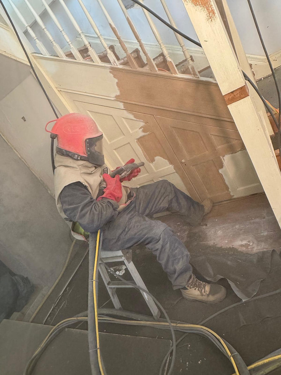 Removing paint by sandblasting from wooden staircase panels to expose natural timber